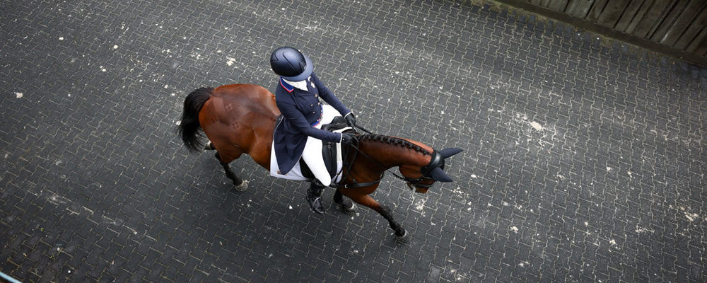 Overhead shot of Caroline Pamukcu riding a horse on a paved track.