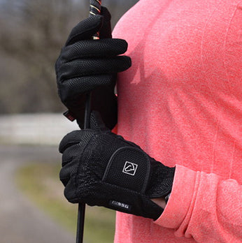 Person wearing black gloves holding a golf club with a blurred natural background